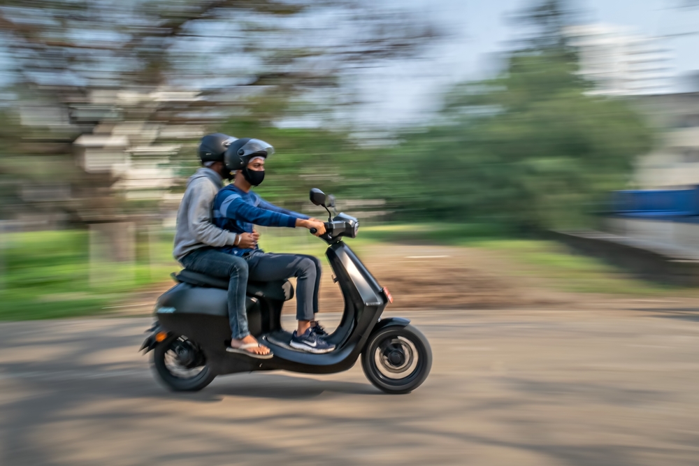 Slow shutter, Motion blur image of a men wearing helmets for safety, riding on a blue electric scooter.
