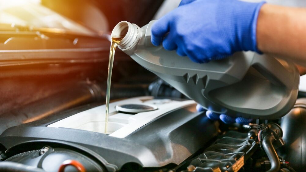 Close up of professional mechanic who is pouring engine oil in the car engine