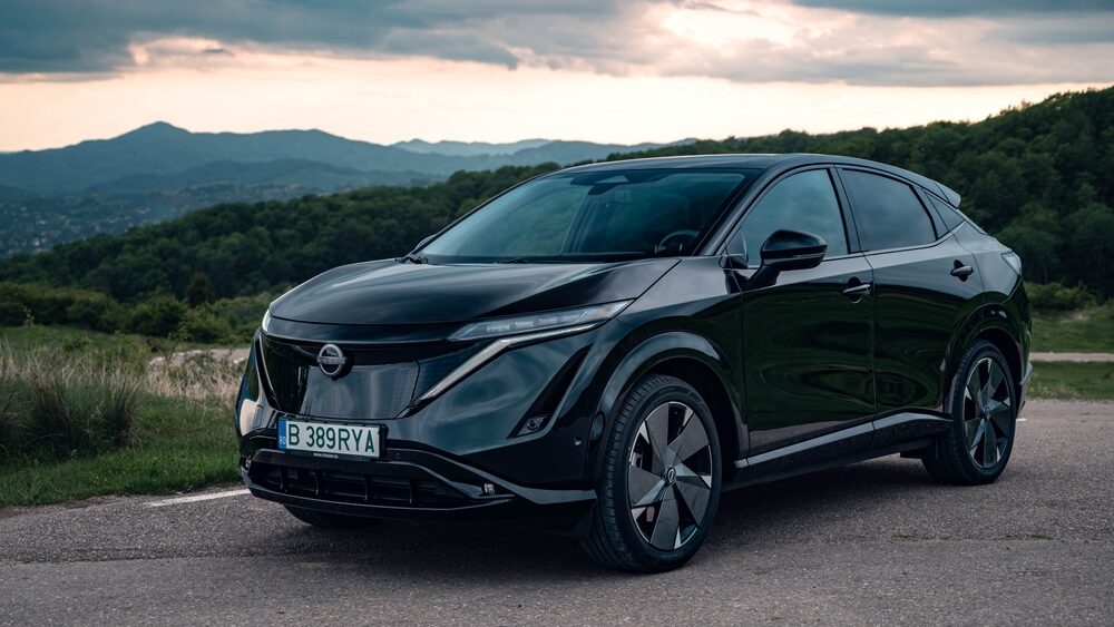 Nissan Ariya in black color, parked roadside with mountains in the background