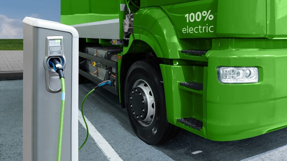 Electric truck being charged from power cable on charging station representing the rise of electric trucks