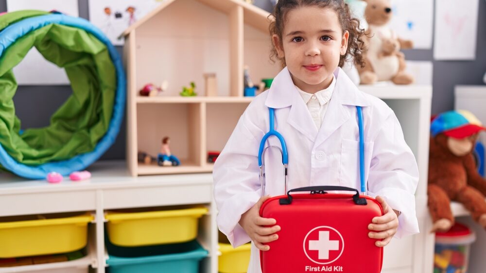 Adorable hispanic girl wearing doctor uniform holding first kit aid at kindergarten