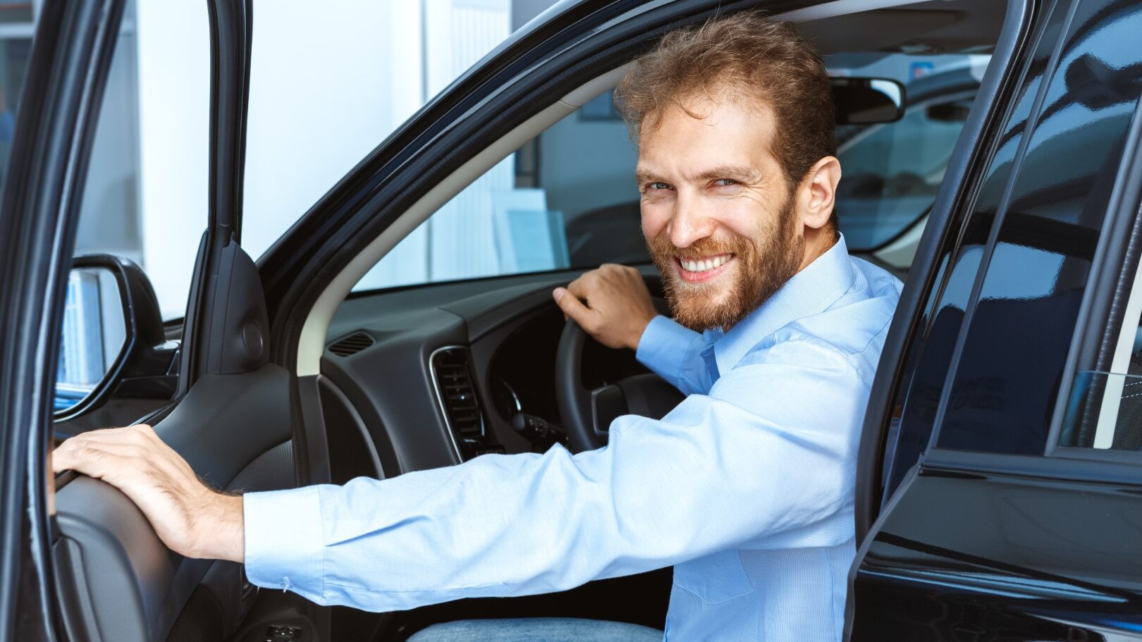 Man smiling while sitting in the car and holding the door open